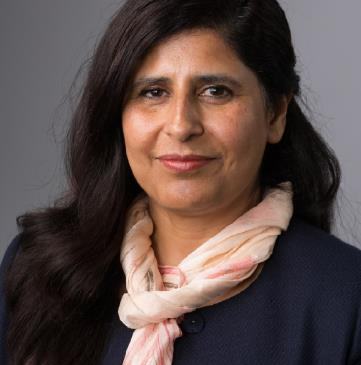 Headshot of a woman with long dark hair and a light patterned scarf, looking at the camera.