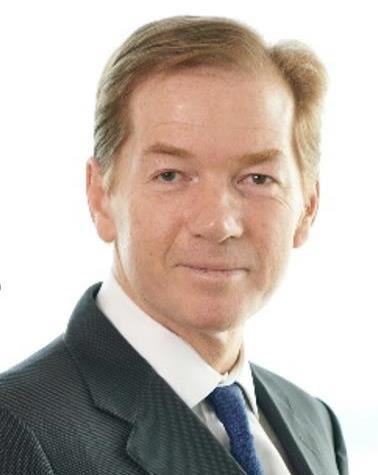 Headshot of a man with light brown hair, wearing a dark suit and a blue patterned tie.