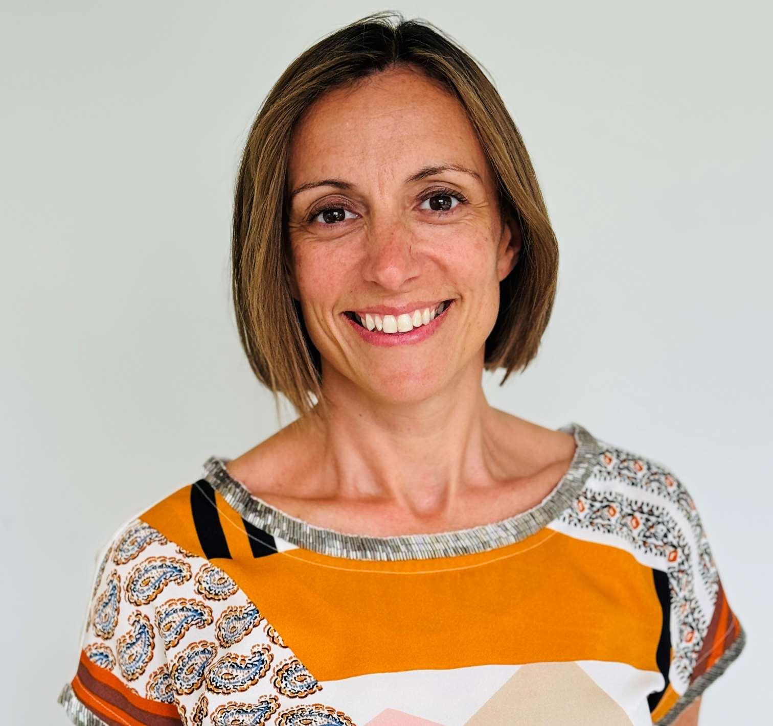 Headshot of a smiling woman with short brown hair, wearing a colorful patterned top.