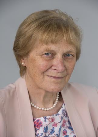 Portrait of an older woman with short blonde hair, wearing a pearl necklace and a light pink blazer, smiling slightly.