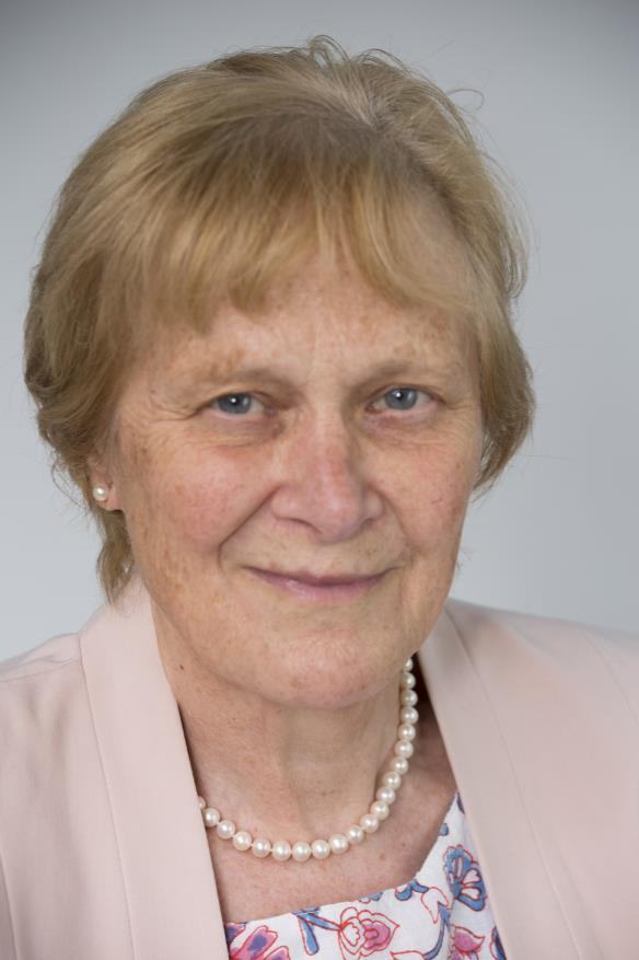 Headshot of an older woman with light hair, wearing a pearl necklace and a pink jacket, smiling.