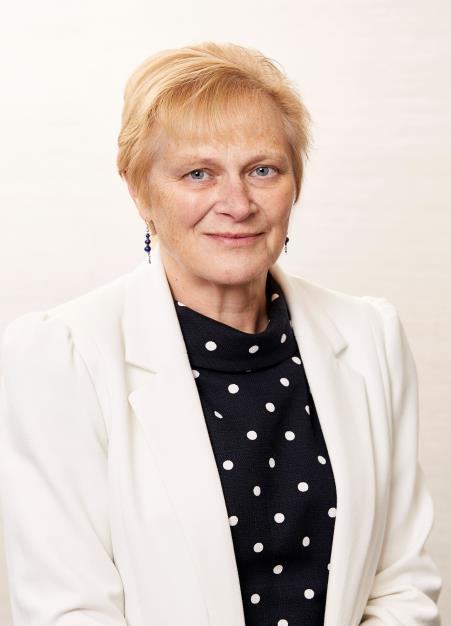 Headshot of a woman with short blonde hair, wearing a white blazer and a black polka-dot top, smiling.